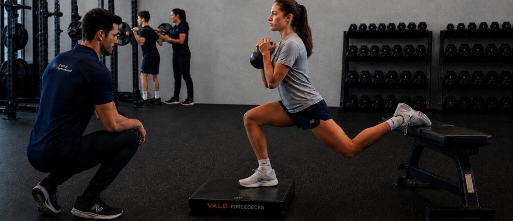 Strength training for young athletes — teenage athlete performing a heavy barbell back squat, supervised by a Central Performance physio coach in Sydney, Surry Hills